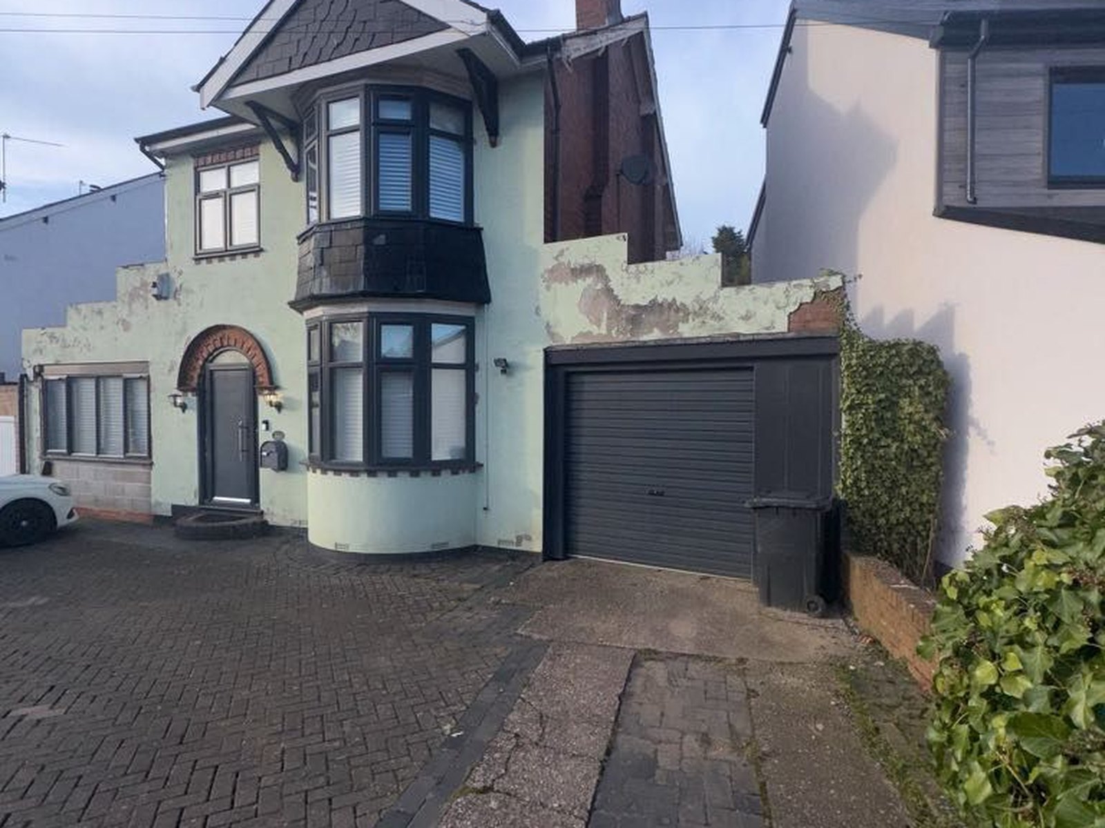 Detached house with cracked and peeling green painted render before the work